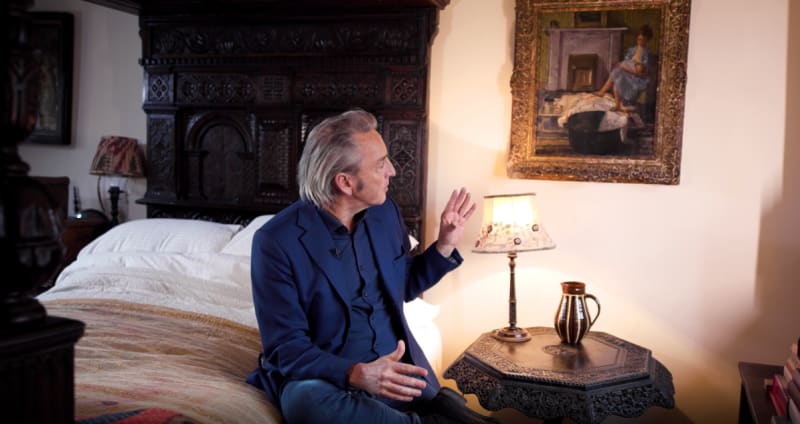 Philip Mould on a four poster bed looking at an impressionist painting