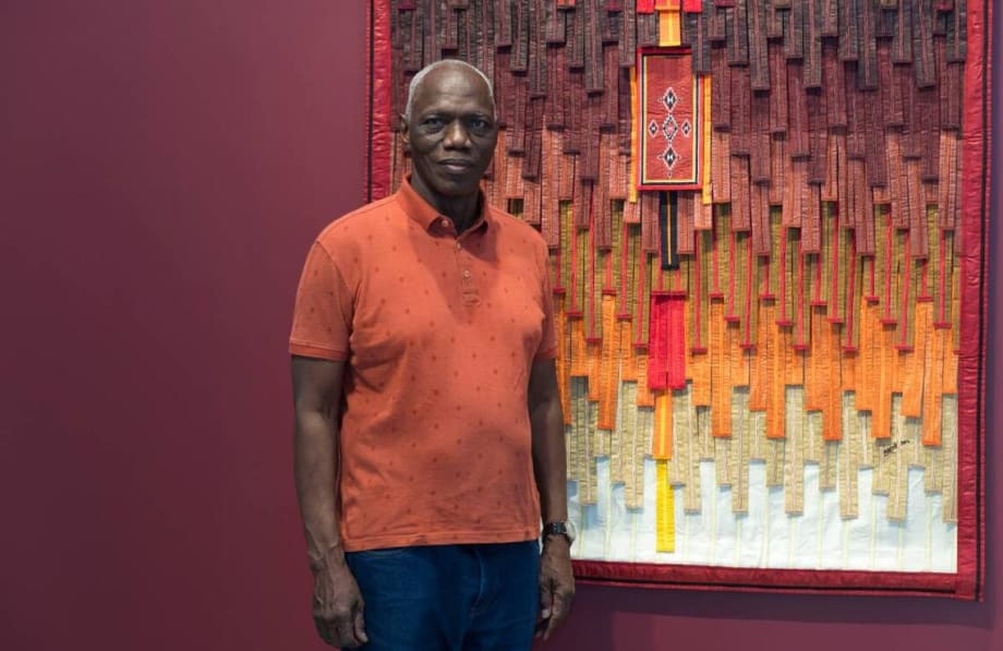 Portrait de l'artiste devant son oeuvre : Motif Arkila kerka-tiangles et carrés sur fond ocre, 2024, GALERIE FARAH FAKHRI