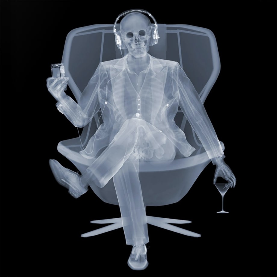 Nick Veasey x-ray photograph "Easy Listener" of a man sitting in a chair with headphones on, wine in one and and a phone in the other