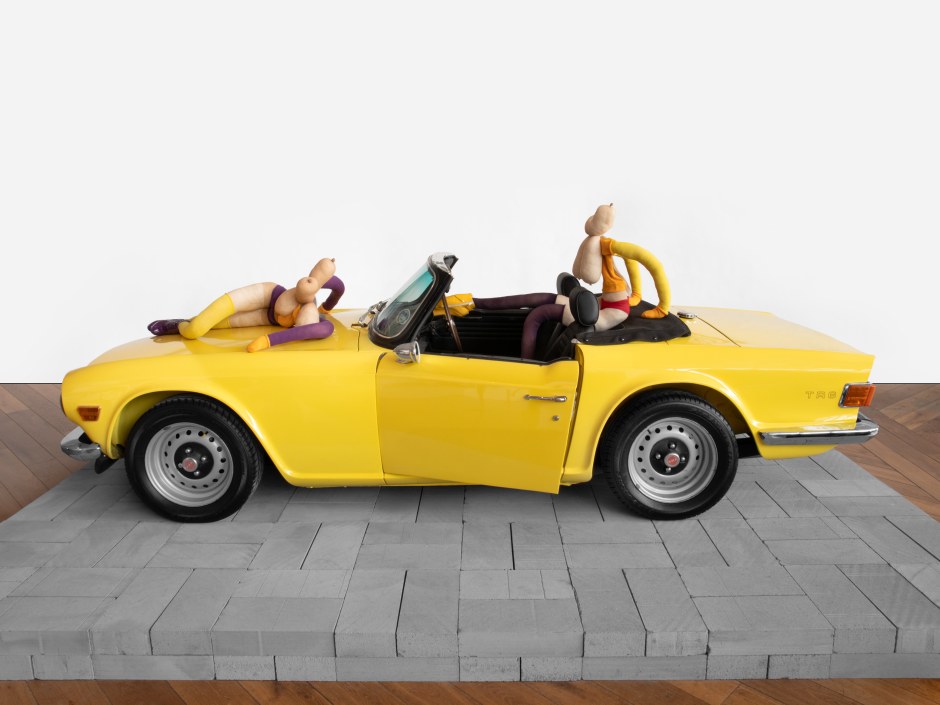 Sarah Lucas  SIX CENT SOIXANTE SIX, 2023  Triumph TR6, tights, wire, wool, shoes, acrylic paint, wigs, breeze blocks  overall size: 207 x 400 cm / 81 ½ x 157 ½ in red bunny: 120 x 55 x 128 cm / 47 ¼ x 21 ⅝ x 50 ⅜ in purple bunny: 35 x 156 x 105 cm / 13 ¾ x 61 ⅜ x 41 ⅜ in car: 118 x 148 x 400 cm / 46 ½ x 58 ¼ x 157 ½ in plinth: 20 x 440 x 220 cm / 7 ⅞ x 173 ¼ x 86 ⅝ in  © Sarah Lucas. Courtesy the Artist and Sadie Coles HQ, London.  Photo: Katie Morrison