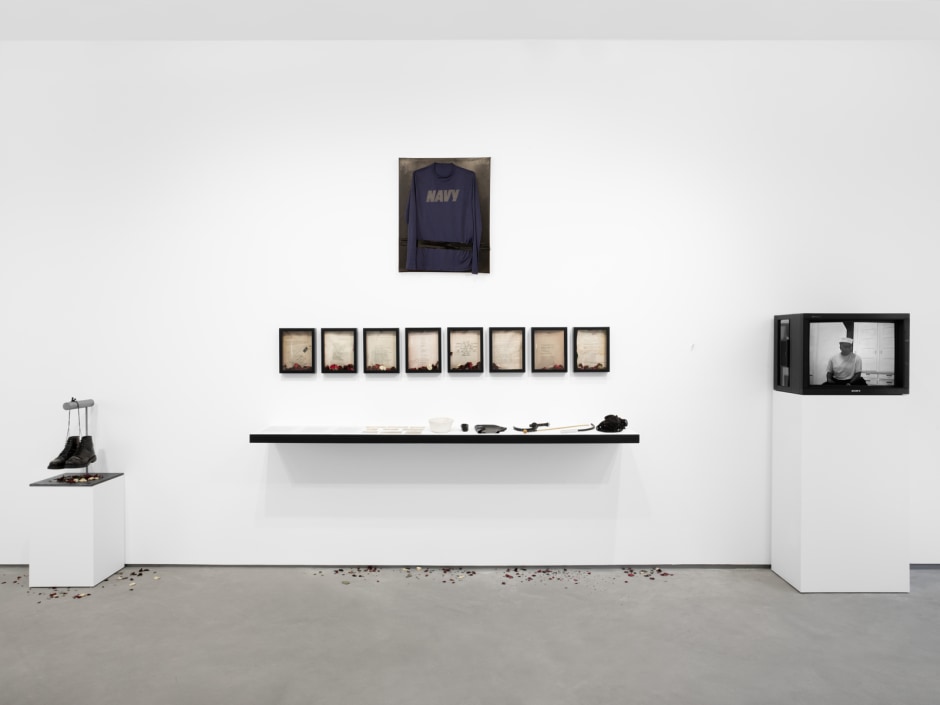 Tiona Nekkia McClodden  The Brad Johnson Tape [REPAIR], 2017 – 2022  Kiwi shoe polish, leather boots, leather dye, steel fixture, blood, sweat and tears on handcut leather, black dye on artist's wood frame, eight inkjet prints in shadowbox frames, inkjet print of 3 page document, digital photo prints, Navy issue sailor hat, leather arm band, ball gag, rzor, nostril breathing rubber mask, caning stick, rubber flagellation tool with metal handle, 100 ft black cotton rope, VHS + HD color/bw with sound, dried roses  overall dimensions: 279 x 545 x 48 cm / 109 ⅞ x 214 ⅝ x 18 ⅞ in boots: 35.6 x 22.9 x 30.5 cm / 14 x 9 x 12 in t shirt: 76.2 x 61 x 4.4 cm 30 x 24 x 1 ¾ in 8 shadowbox frames; each: 30.5 x 24.1 x 6 cm / 12 x 9 ½ x 2 ⅜ in video dur: 15 min  © Tiona Nekkia McClodden, courtesy Sadie Coles HQ, London  Photo: Katie Morrison